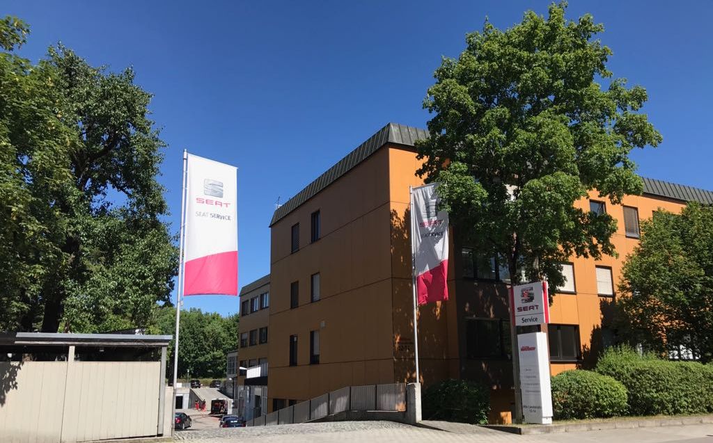 Einfahrt zu Auto Weber von der Straße, mit Fahnen vor dem Gebäude